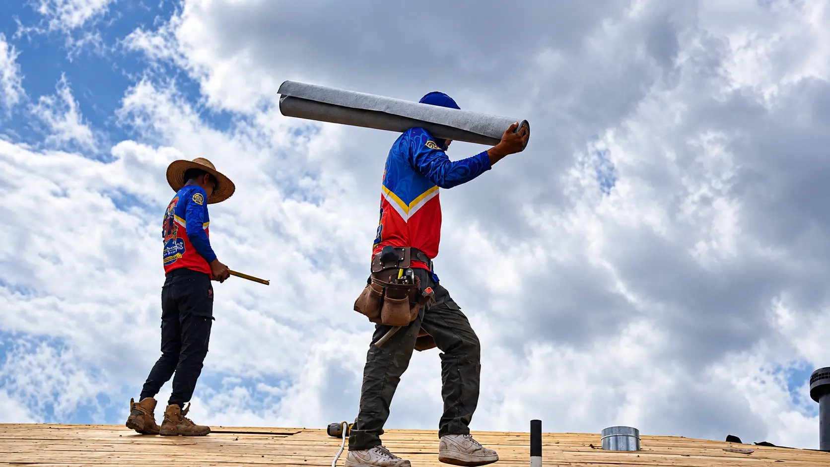 Roofer carrying a roll of underlayment across the roof deck
