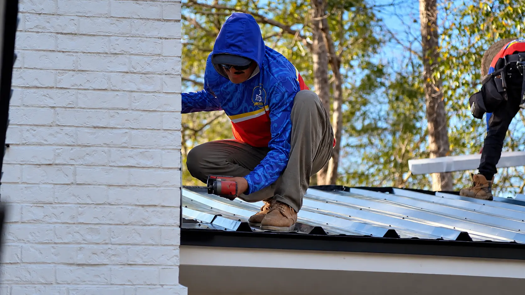 Roofer fastening metal roof panels beside a chimney