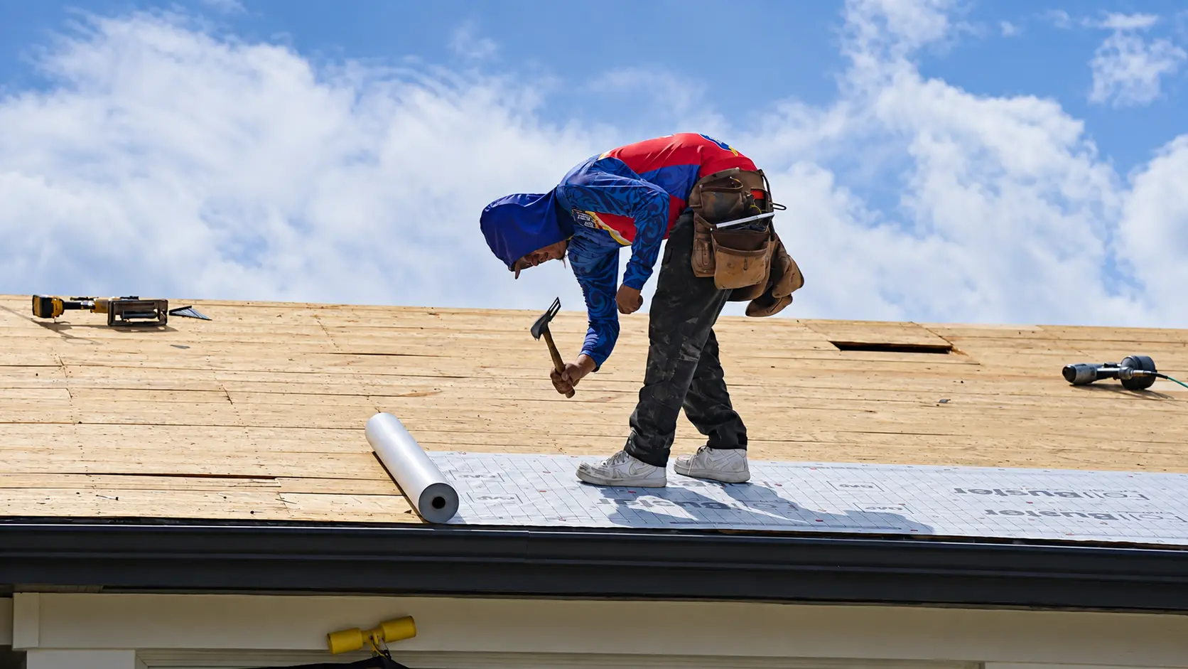 Roofer installing synthetic underlayment on a bare roof deck