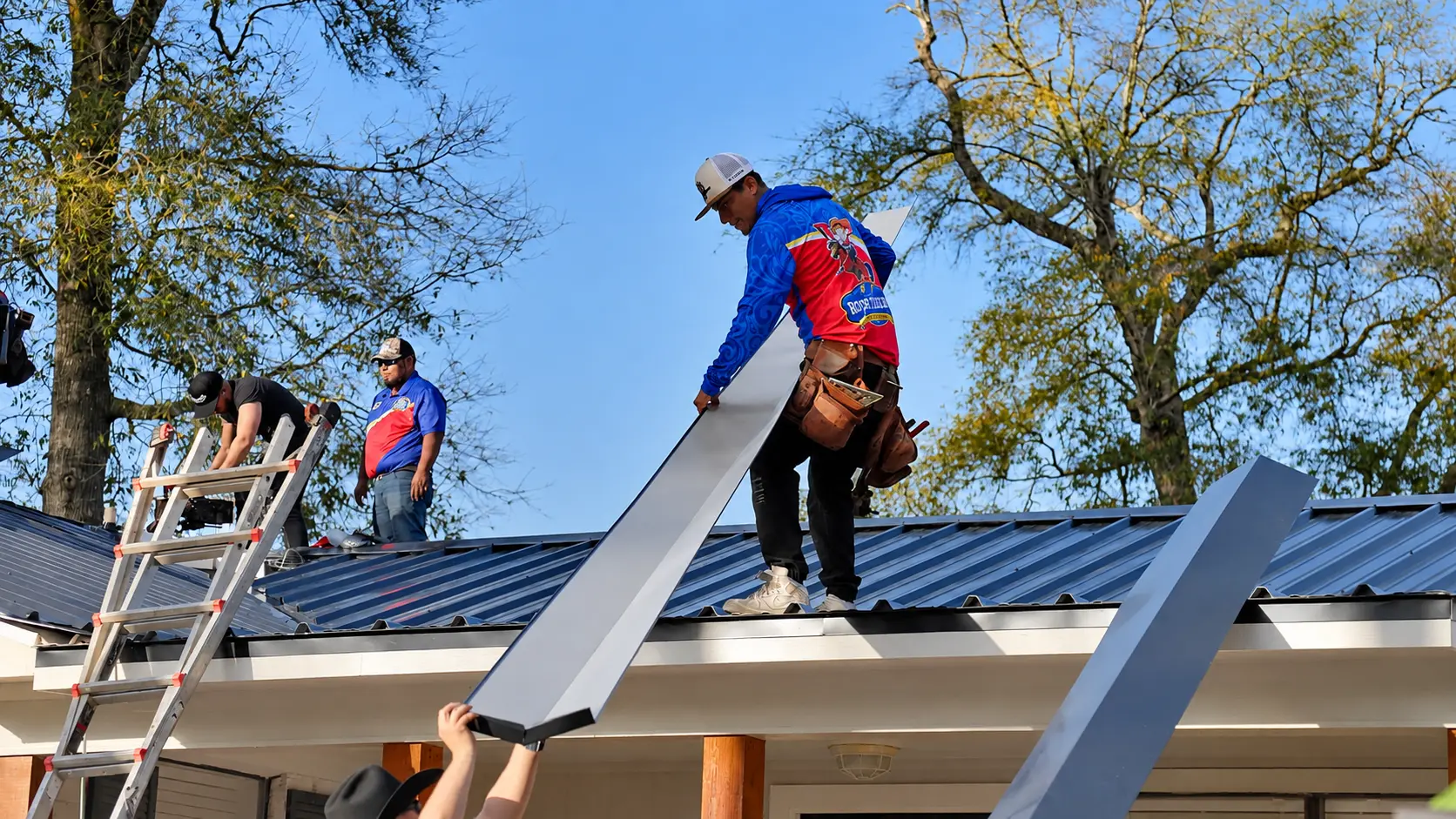 Roof Ryders crew carrying metal roof panels onto the roof